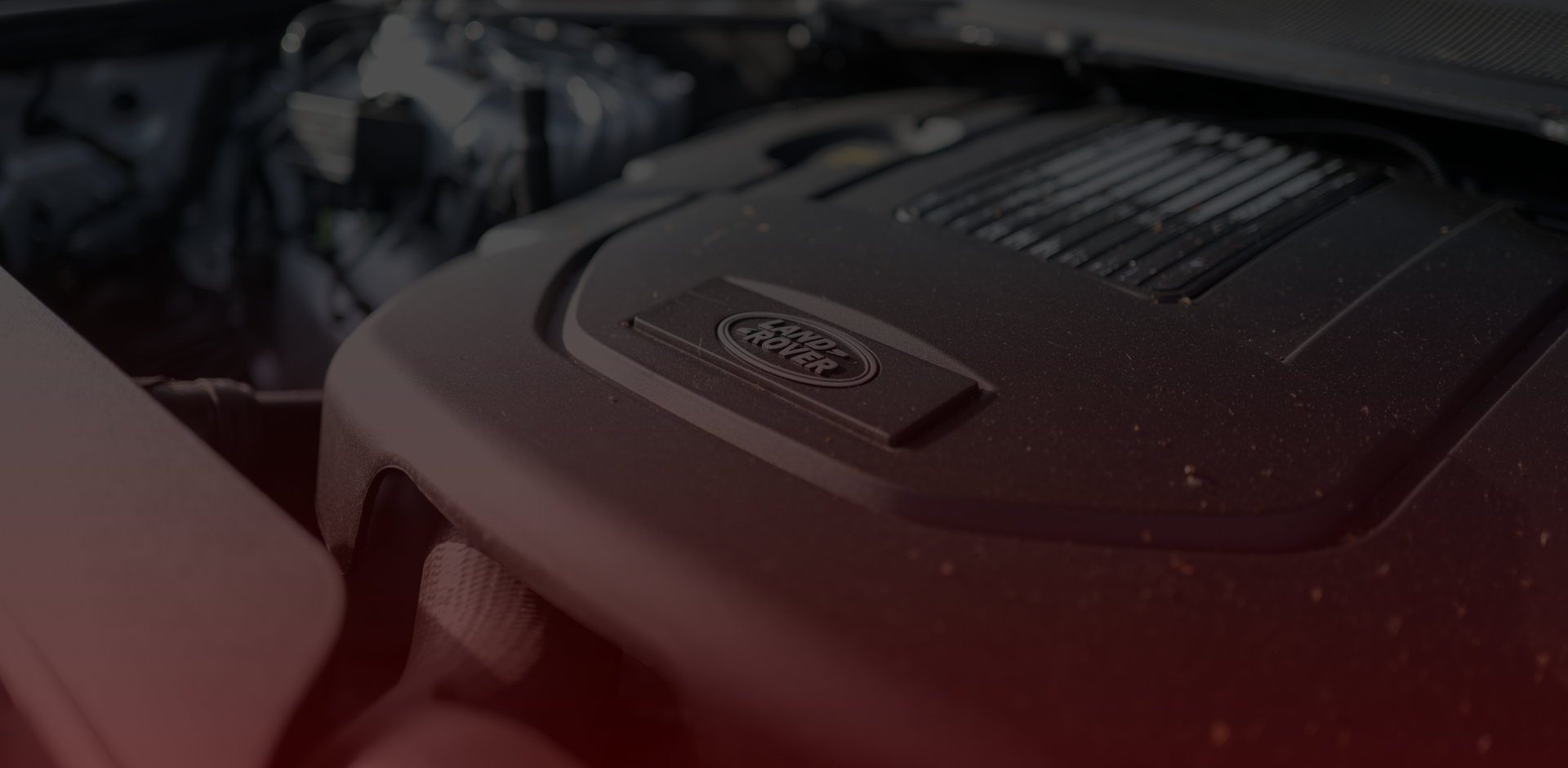 Close-up of a vehicle engine bay, highlighting the Land Rover logo on a black engine cover. The surface has a few specks of dirt, hinting at its rugged journey through Greater Toronto. Other engine components loom in the background, creating a dark, shadowed atmosphere perfect for any Land Rover repair enthusiast. EuroMechanic | Top Reviewed Auto Repair Shop | Greater Toronto and Guelph | Visit Euromechanic