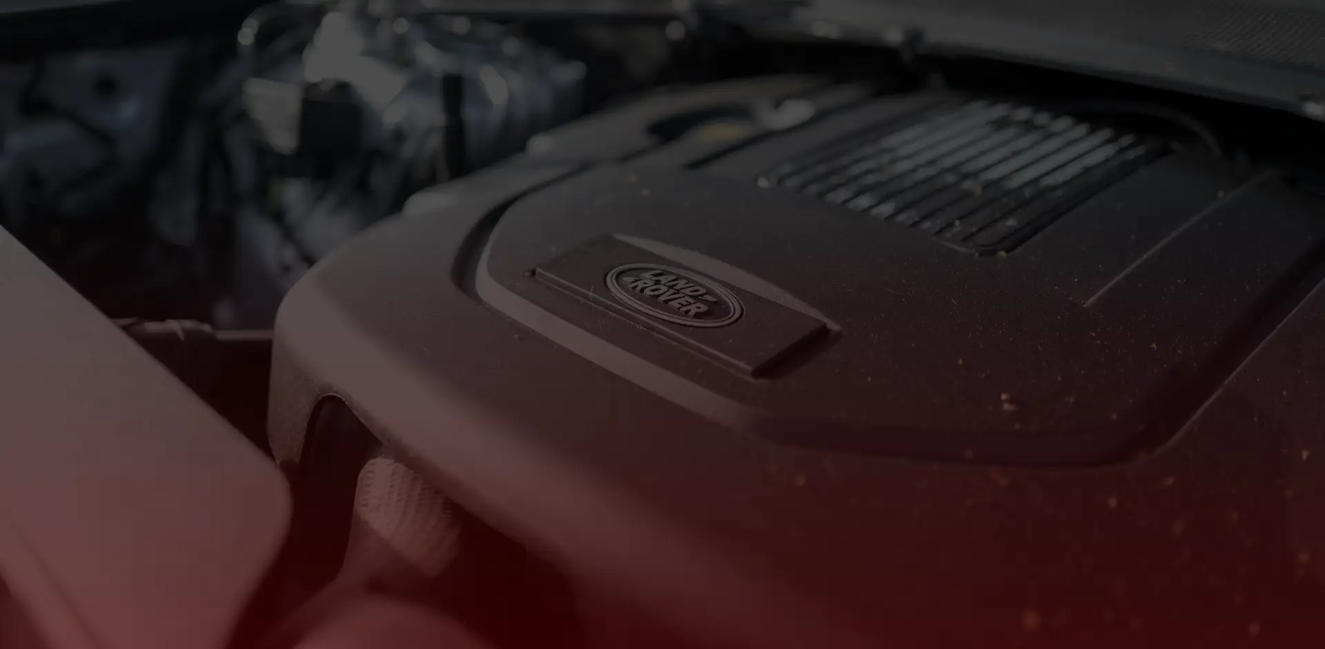 Close-up of a vehicle engine bay, highlighting the Land Rover logo on a black engine cover. The surface has a few specks of dirt, hinting at its rugged journey through Greater Toronto. Other engine components loom in the background, creating a dark, shadowed atmosphere perfect for any Land Rover repair enthusiast. EuroMechanic | Top Reviewed Auto Repair Shop | Greater Toronto and Guelph | Visit Euromechanic