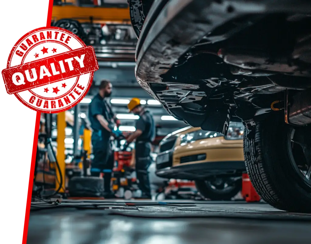 In a bustling Automotive EuroMechanic garage, skilled car mechanics diligently focus on the underside of a vehicle. A Quality Guarantee stamp is prominently featured in the image, highlighting their commitment to excellence. EuroMechanic | Top Reviewed Auto Repair Shop | Greater Toronto and Guelph | Visit Euromechanic