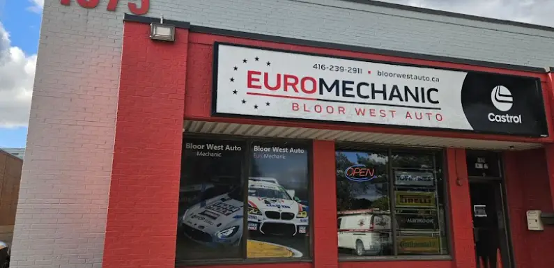 Storefront of Euro Mechanic Bloor West Auto. Features a red and white sign with contact details and logos. The window displays racing car images and an Open sign. Located at 1075, this welcoming location prominently showcases the Castrol logo. EuroMechanic | Top Reviewed Auto Repair Shop | Greater Toronto and Guelph | Visit Euromechanic