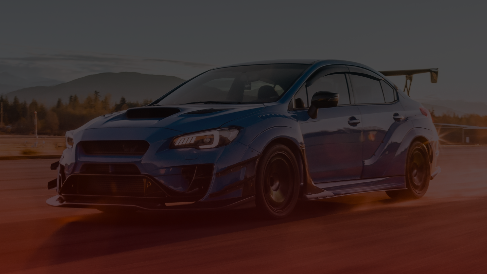 A blue sports car, reminiscent of a skilled Subaru mechanics craftsmanship in Greater Toronto, speeds along a road with a large rear spoiler. Against scenic mountains and trees under a clear sky, its aggressive styling boasts a hood scoop and aerodynamic features. EuroMechanic | Top Reviewed Auto Repair Shop | Greater Toronto and Guelph | Visit Euromechanic