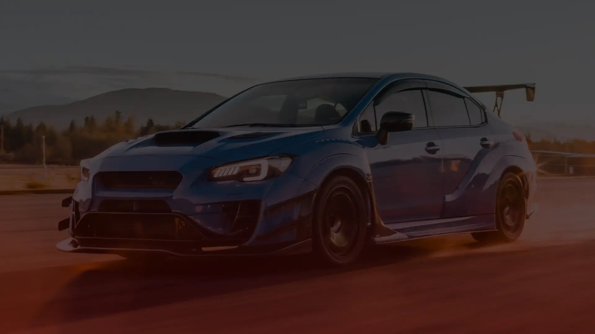 A blue sports car, reminiscent of a skilled Subaru mechanics craftsmanship in Greater Toronto, speeds along a road with a large rear spoiler. Against scenic mountains and trees under a clear sky, its aggressive styling boasts a hood scoop and aerodynamic features. EuroMechanic | Top Reviewed Auto Repair Shop | Greater Toronto and Guelph | Visit Euromechanic