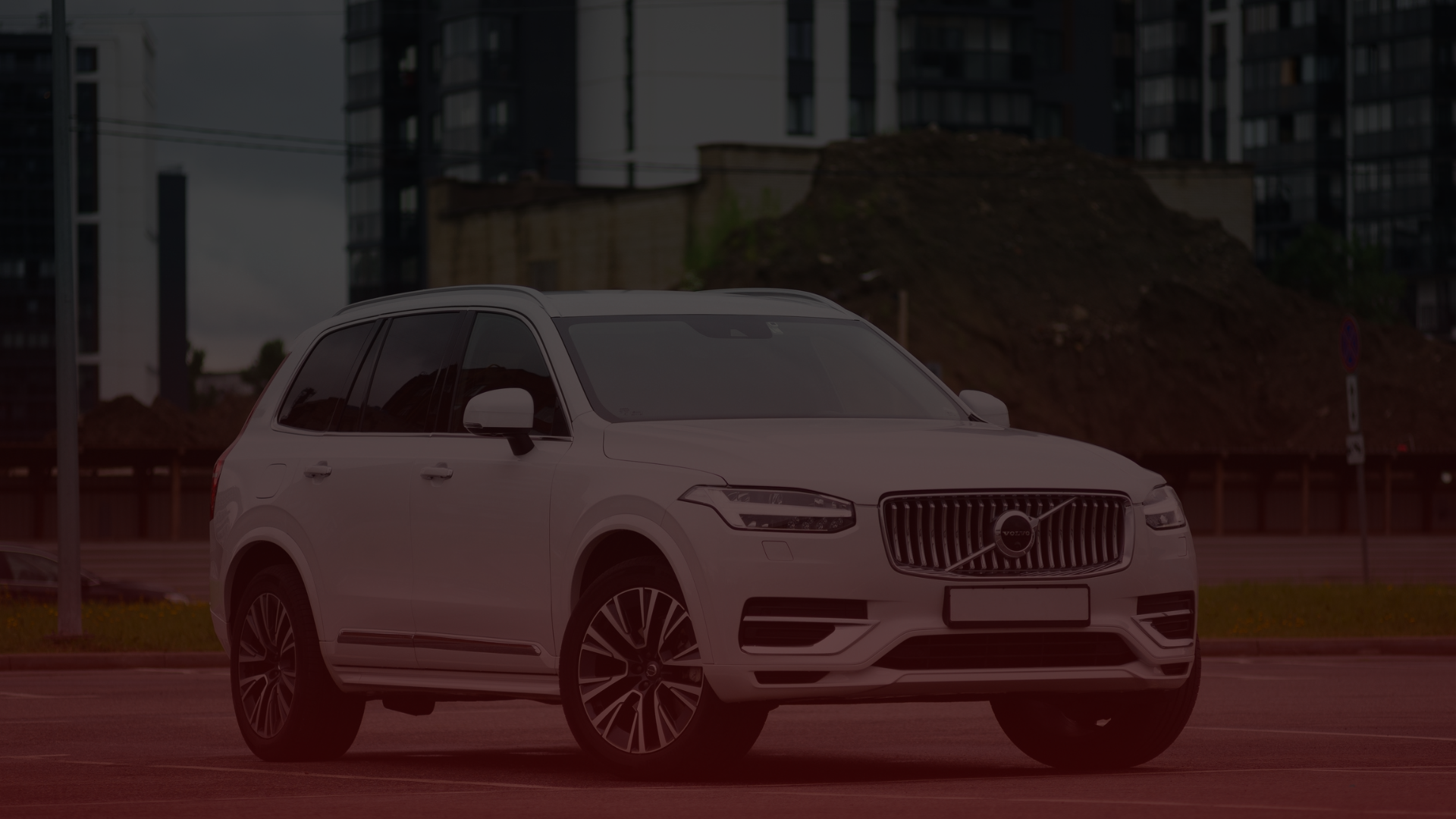 A white Volvo SUV is parked in an open area, against a backdrop of modern buildings and a pile of dirt. With its sleek design and chrome detailing, this vehicle captures attention, much like the trusted Volvo mechanics across Greater Toronto and Guelph that keep it running flawlessly. EuroMechanic | Top Reviewed Auto Repair Shop | Greater Toronto and Guelph | Visit Euromechanic